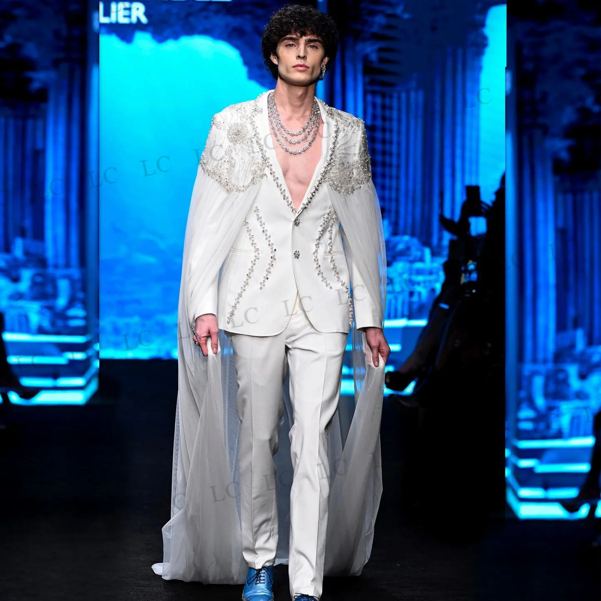 Costume homme blanc orné de perles, avec cape transparente et collier superposé 