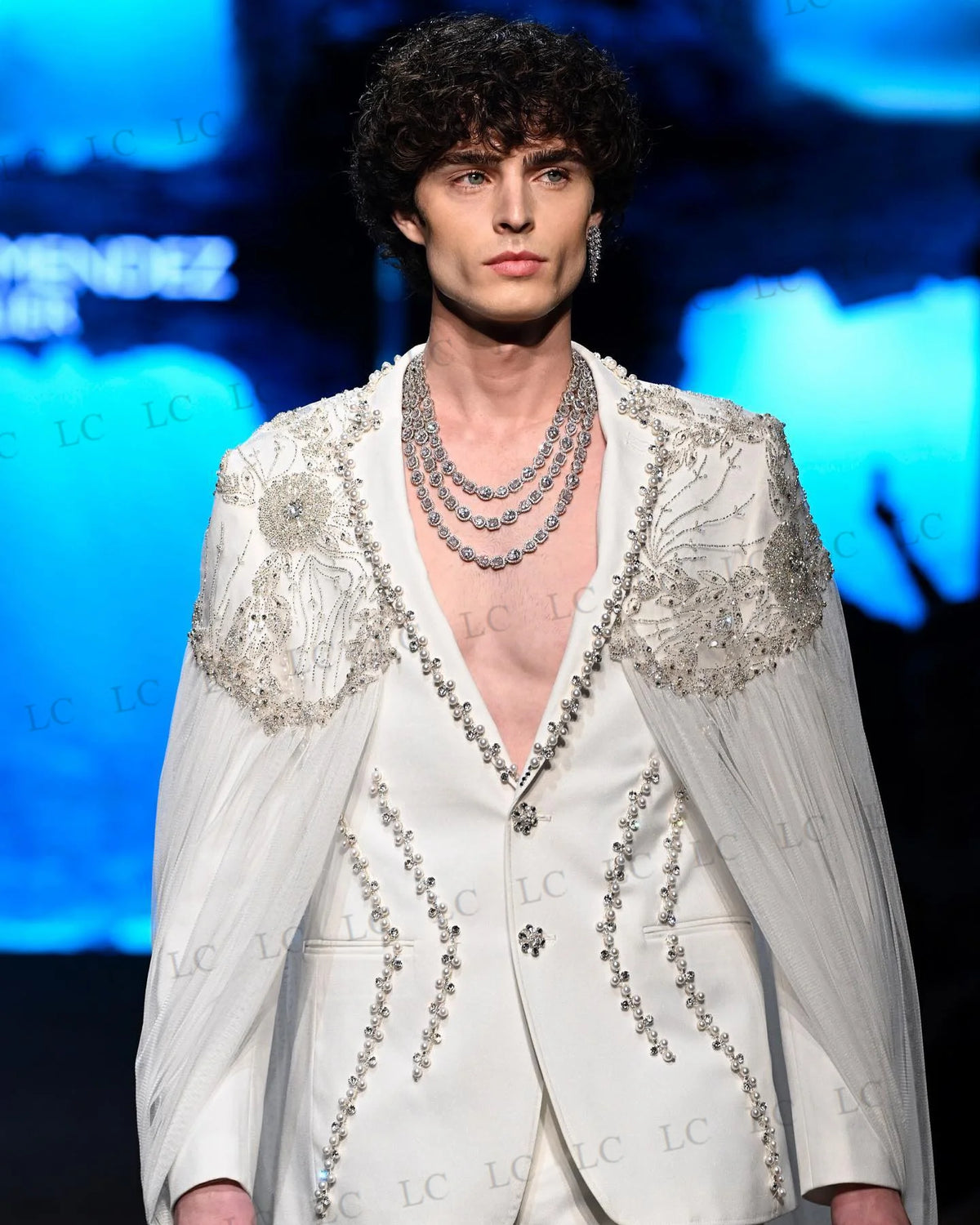 Costume homme blanc orné de perles, avec cape transparente et collier superposé 