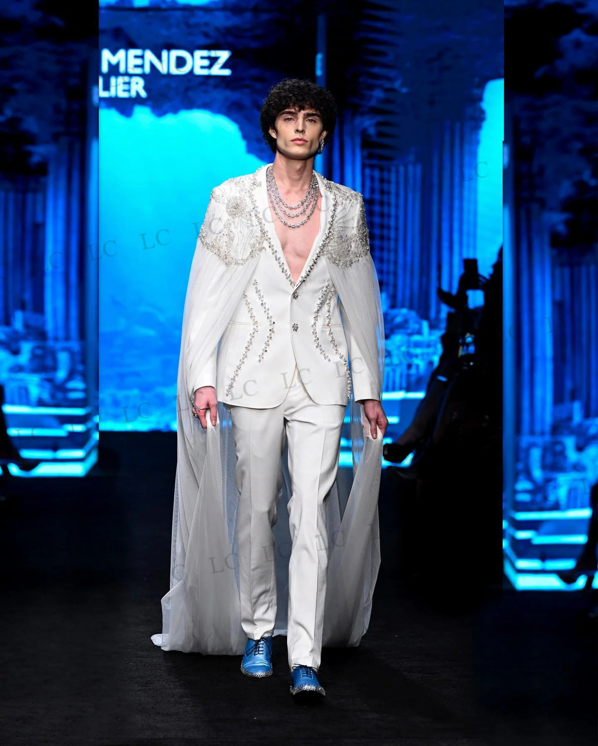 Costume homme blanc orné de perles, avec cape transparente et collier superposé 